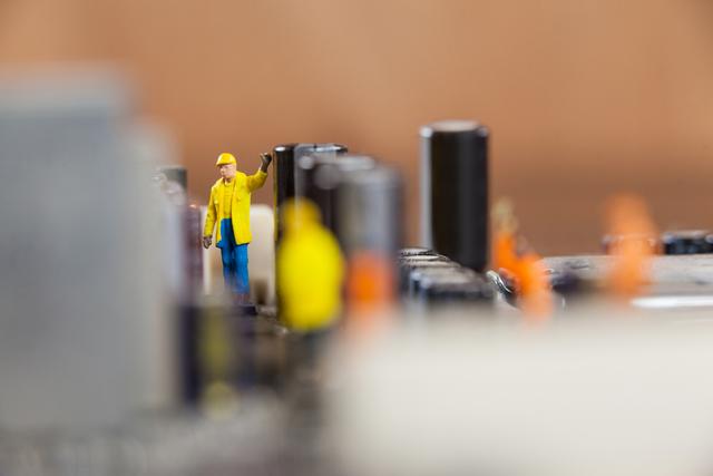Conceptual image shows miniature toy workers engaged in activities on a large motherboard chip, highlighting themes of technology, engineering, and teamwork. Ideal for educational materials, engineering and technology advertisements, and creative conceptual art projects.