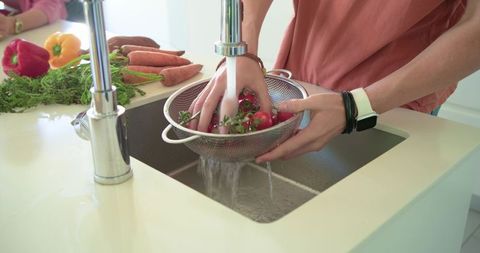 Washing fresh radishes and herbs in colander under running faucet on modern kitchen countertop