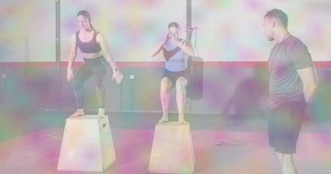 Women jumping on plyo boxes while trainer observing during high-intensity gym workout