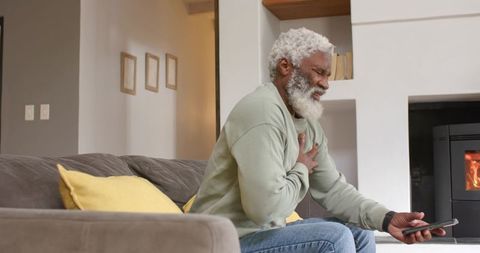 Senior man holding chest in discomfort on modern sofa
