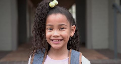Cheerful schoolgirl smiling confidently at entryway with backpack