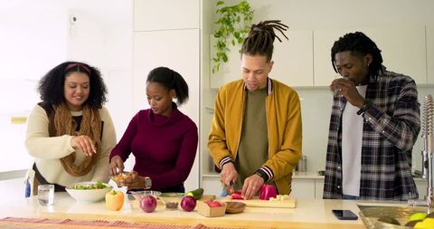 Multiracial friends preparing fresh salad at modern kitchen island with cutting board
