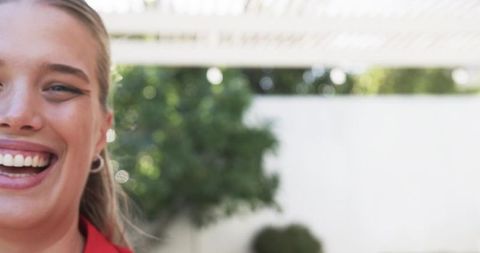 Young woman smiling on sunlit patio wearing red jacket and silver hoop earring