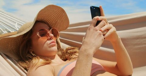 Woman Relaxing in a Hammock on Beach Using Mobile Phone