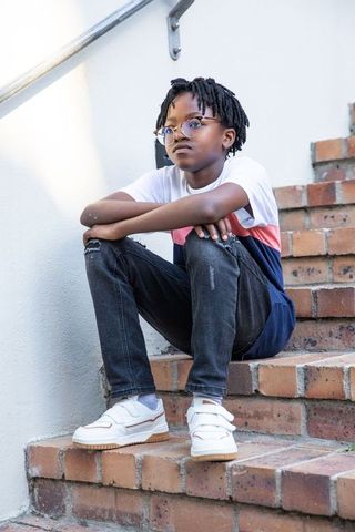 Contemplative boy with glasses sitting on outdoor steps in casual attire