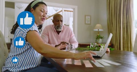 Couple collaborating on paint swatches at dining table with laptop and social like icons