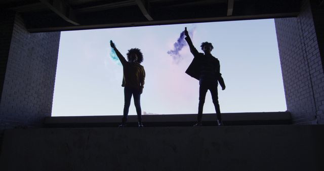 Silhouettes of Two Young Individuals Holding Smoke Flares in Urban Location - Download Free Stock Images Pikwizard.com