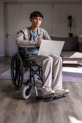 Asian man in wheelchair using laptop at home office showcasing accessibility, independence