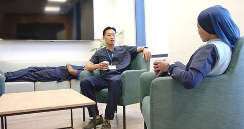 Diverse medical staff taking coffee break in modern staff lounge, chatting and sipping coffee