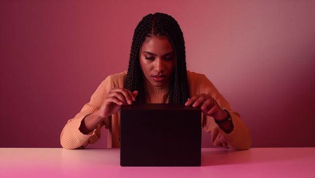 Woman opening mysterious black box on white table in pink ambient