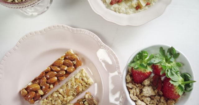 Appealing composition of nutritious breakfast items including granola bars with almonds, a bowl of cereal mixed with strawberries and nuts, and a bowl of oatmeal with assorted nuts and fruit. Perfect for illustrating healthy eating habits, breakfast menus, nutrition guides, or wellness blogs.