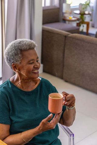 Senior african american woman smiling holding peach mug in cozy living room