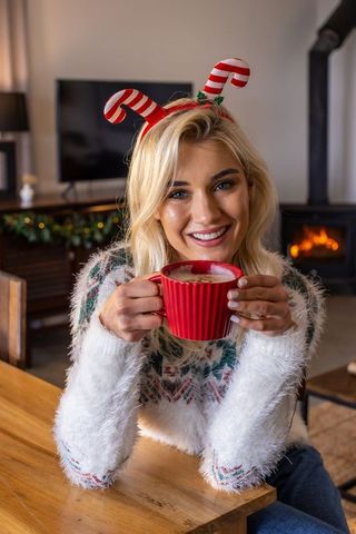 Cozy holiday morning smiling woman holding red ribbed mug wearing candy-cane headband