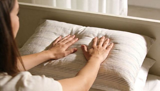 Woman pressing palms onto striped pillow on bed, smoothing linen bedding in morning light