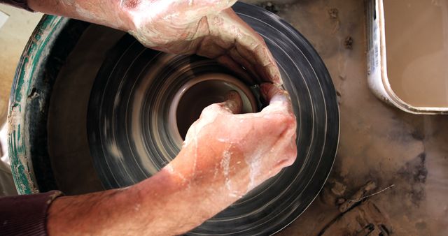 Close-up view of a potter's hands shaping clay on a spinning potter's wheel. Perfect for illustrating creative processes, artistic endeavors, and traditional craftsmanship. Useful for articles about handmade crafts, pottery workshops, and artists at work. Ideal for motivational materials emphasizing creativity and skill.