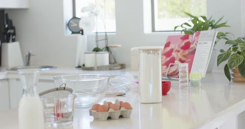Sunlit kitchen countertop preparing baking ingredients with eggs, mixing bowl, whisk