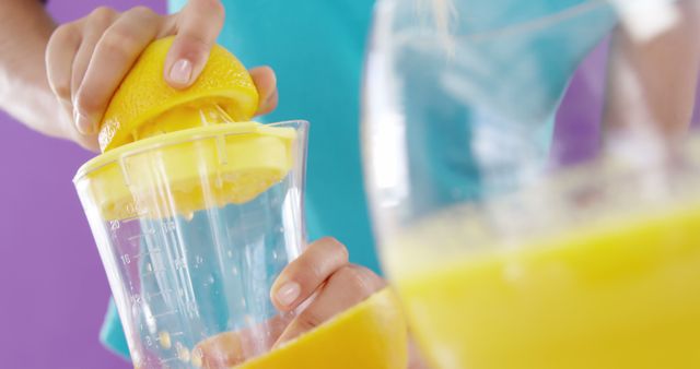 Close-up of person squeezing fresh lemon juice into a clear measuring cup, showing a bright and refreshing yellow color. Ideal for use in content related to healthy eating, recipes, cooking demonstrations, and natural beverages.