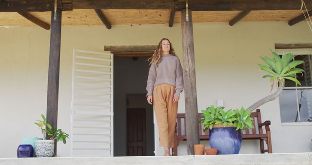 Smiling caucasian woman standing, leaning outside house looking out from terrace. healthy living, close to nature in off grid rural home.