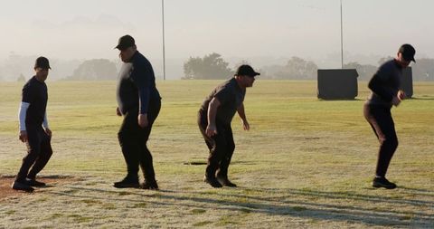 Teammates Practicing Drill at Dawn on Dewy Grass Wearing Caps and Dark Gear