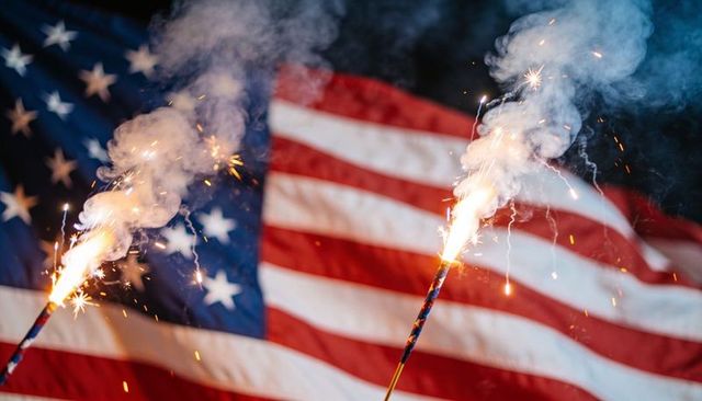 Sparking handheld sparklers with waving american flag celebrating fourth of july night