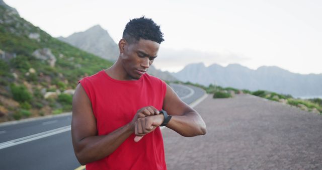 African american man using fitness band while standing on the road. fitness sports and healthy lifestyle concept