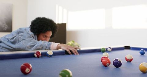 African american man leaning over blue-felt pool table lining up shot in home gameroom