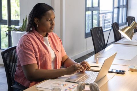 African american woman working on laptop at shared desk, modern coworking productivity