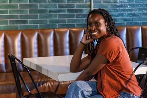 Smiling african american woman sitting in cozy cafe booth with green tile and leather banquette