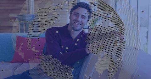 Smiling man leaning on sofa with dotted globe overlay for digital connectivity concept
