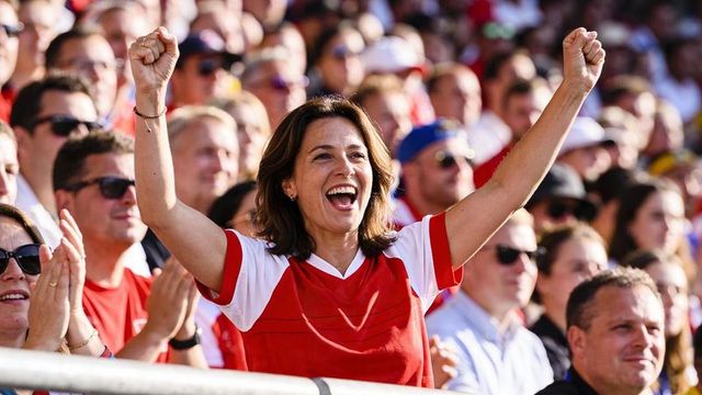 Female fan cheering and raising arms in red and white jersey at outdoor stadium crowd