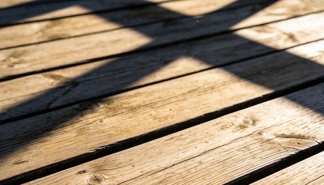 Weathered Wooden Deck Planks Showing Grain, Knots, Gaps and Dramatic Diagonal Shadows