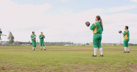 Diverse female softball team practicing on field in uniforms