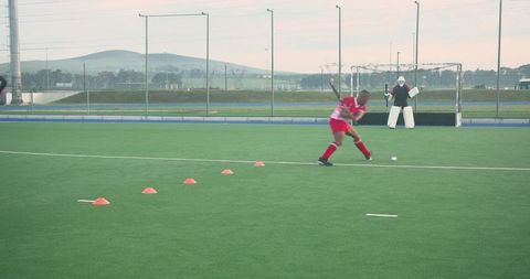 Field hockey player dribbling ball around cones at outdoor field