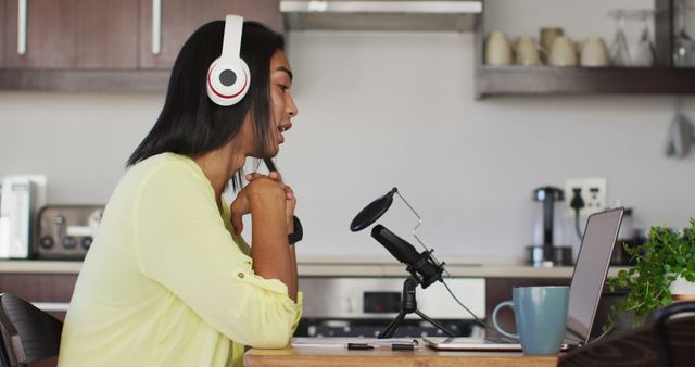 Woman is recording a podcast from her home using a microphone and headphones, while working on a laptop. Great for use in articles about remote work, podcasting, digital content creation, modern technology, or studying from home. Ideal for illustrating blog posts, online courses, tutorials, social media content, and promotional materials related to communication and technology.
