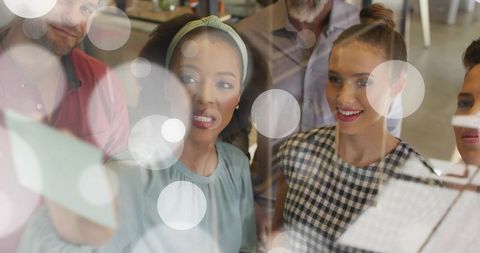 Creative team collaborating around glass board with sticky notes and bokeh overlay