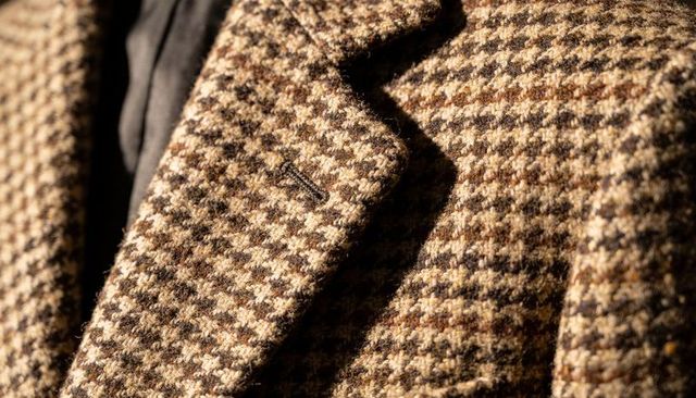 Close-up showing houndstooth wool coat lapel revealing textured woven fabric and stitched buttonhole