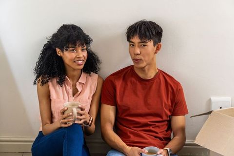 Young black woman and asian man sitting on floor drinking coffee during relaxed move-in moment