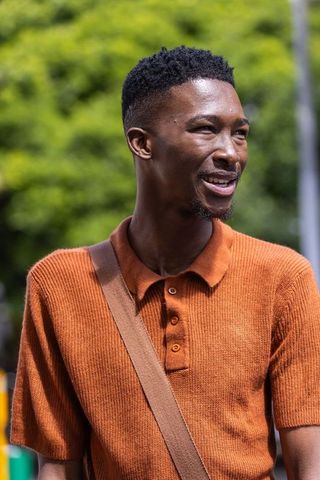Young man smiling and speaking outdoors wearing rust orange polo and brown crossbody bag