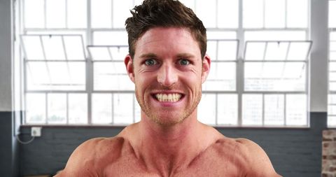 Smiling Muscular Man Flexing in Modern Gym
