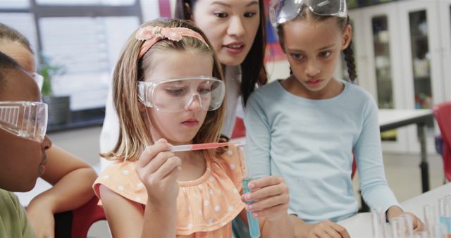 Image depicts young students conducting a science experiment in a classroom under the guidance of their teacher. They are wearing safety goggles and using laboratory equipment. Ideal for educational websites, STEM programs promotions, and science-related learning materials.
