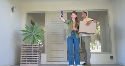 Young diverse couple moving into new home taking selfie on modern front porch