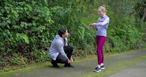 Runners pausing on mossy trail, man tying shoe while woman checking fitness watch