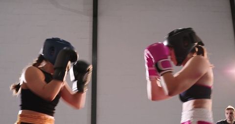 Female boxers sparring in ring wearing headgear and gloves showing training intensity and focus