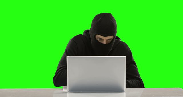 Masked Hacker Operating on Laptop with Green Background - Download Free Stock Images Pikwizard.com