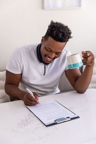 African american man signing documents at modern marble table while holding coffee mug