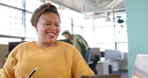 Smiling woman in mustard sweater collaborating with team in bright modern open office