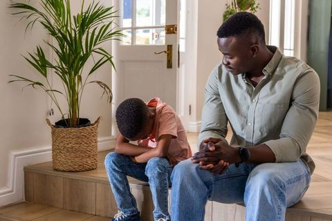 African american father comforting sad son sitting on home steps near front door