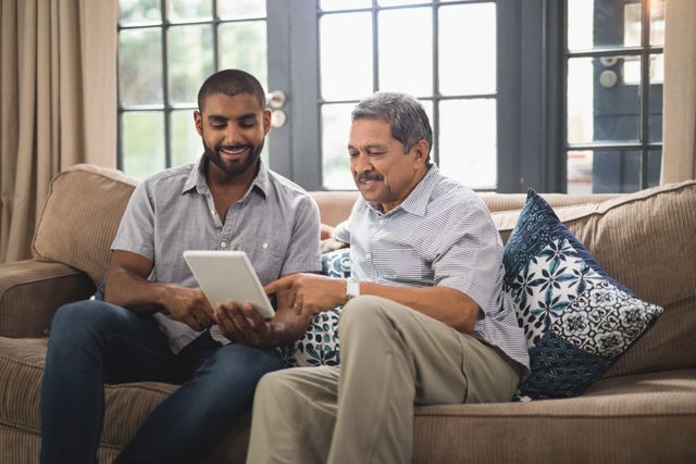 Smiling man with his father using digital tablet while sitting together on couch at home