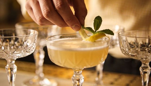 Bartender garnishing lemon peel and mint on crystal coupe cocktail with foam