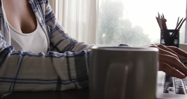 Person Typing on Laptop Indoors Near Window with Coffee Mug - Download Free Stock Images Pikwizard.com